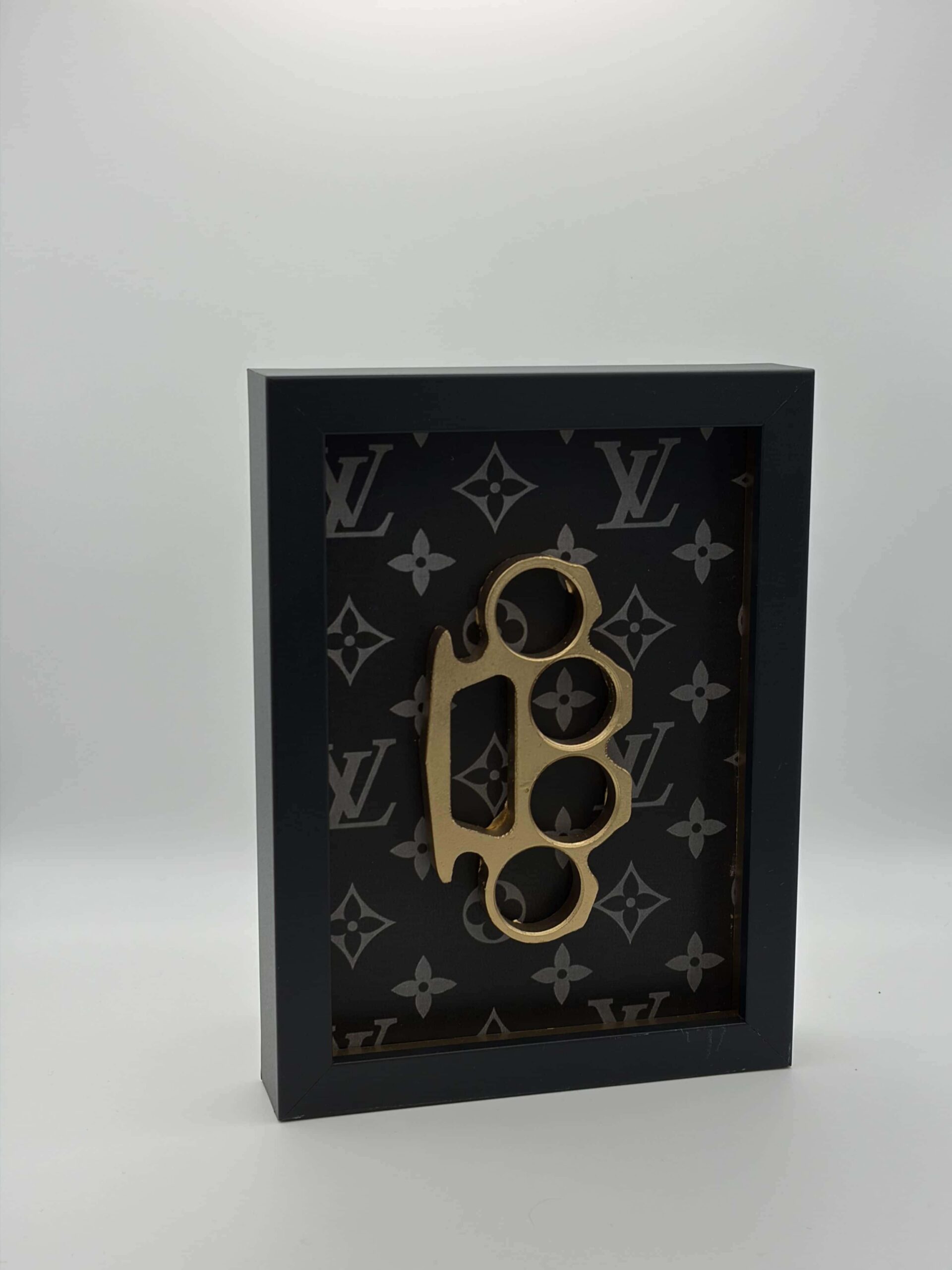 Quadro d'arredamento moderno con icone 3D in oro, pistola, lingotto e tirapugni su sfondo monogram luxury.